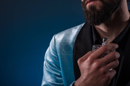 Photo for Beautiful masculine bearded young man holding a bottle of fragrance. Masculine perfume, bearded man in a suit. - Royalty Free Image