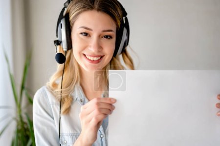 Foto de Hermosa mujer joven con auriculares sosteniendo pedazo de papel ampty - Imagen libre de derechos
