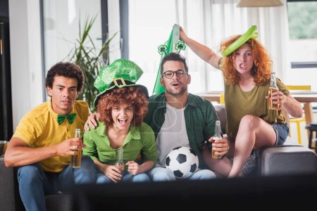Foto de Grupo multiétnico de jóvenes divirtiéndose, viendo un partido de fútbol en la televisión. Animando a Irlanda. - Imagen libre de derechos
