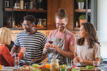 Téléchargez les photos : Jeunes gens diversifiés faisant une fête de vacances à la maison, préparant la nourriture, buvant, parlant et appréciant - en image libre de droit