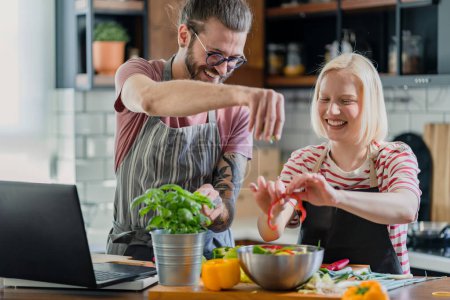 Foto de Joven pareja alegre preparando un almuerzo vegano saludable en casa con computadora portátil - Imagen libre de derechos