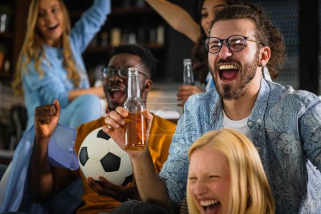Foto de Emocionado grupo de jóvenes multiétnicos viendo un partido de fútbol en un televisor en casa - Imagen libre de derechos