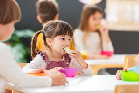 Téléchargez les photos : Les enfants mangent une collation aux fruits dans une maternelle - en image libre de droit