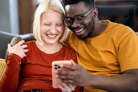 Foto de Feliz pareja multiétnica buscando algo en un teléfono inteligente en el interior - Imagen libre de derechos