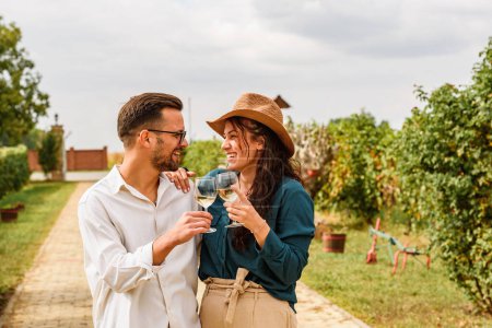 Foto de Joven pareja sonriente degustando vino en el viñedo de la bodega - Concepto de amistad y amor con los jóvenes disfrutando del tiempo de cosecha - Imagen libre de derechos