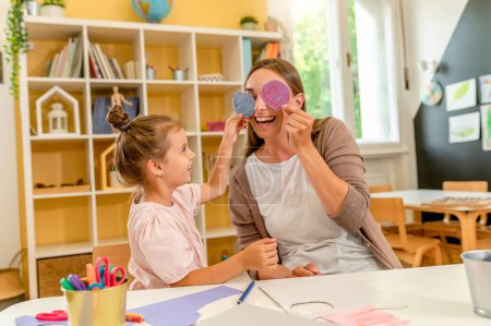 Photo for The teacher helping a child and they are working together making some paper crafts. Developing Fine motor skills for toddlers and preschoolers - Royalty Free Image