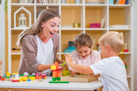 Photo for Kindergarten teacher playing together with children at colorful preschool classroom. Mother playing with children. - Royalty Free Image