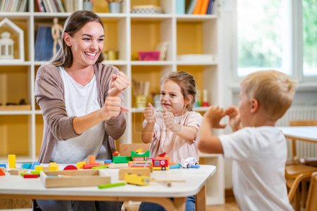 Photo for Kindergarten teacher playing together with children at colorful preschool classroom. Mother playing with children. - Royalty Free Image