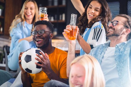 Téléchargez les photos : Groupe excité de jeunes gens multiethniques regardant un match de football à la télévision à la maison - en image libre de droit