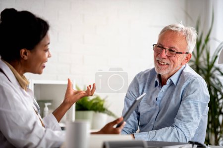 Photo for Doctor specialist consulting a patient in a doctor's office at a clinic. Female doctor is talking with a male elderly patient. - Royalty Free Image