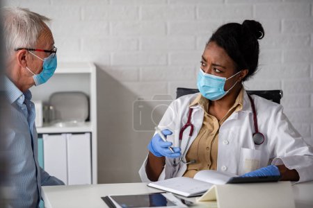 Photo for Female doctor is examining male elderly patient at clinic. Doctor and patient wearing a face masks. - Royalty Free Image