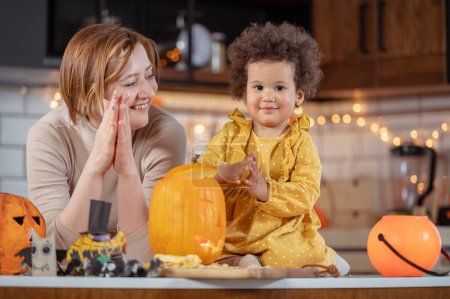 Photo for Mother and cute little daughter having fun with jack -o -lantern in the kitchen. Halloween holiday - Royalty Free Image