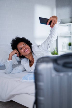 Téléchargez les photos : Jeune femme d'affaires noire vient d'arriver à l'hôtel pour se reposer d'un voyage, à l'aide d'un smartphone - en image libre de droit