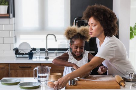 Foto de Madre enseñando a su hijo a cocinar y ayudar en la cocina. Madre e hija afroamericana haciendo galletas en casa. - Imagen libre de derechos
