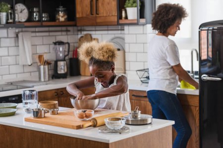Foto de Madre enseñando a su hijo a cocinar y ayudar en la cocina. Madre e hija afroamericana haciendo galletas en casa. - Imagen libre de derechos