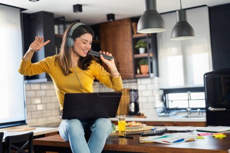 Photo for Young smiling woman with headphones working from home, taking break listening music and singing. Positive emotions. Woman with positive attitude. - Royalty Free Image