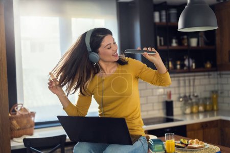 Photo for Young smiling woman with headphones working from home, taking break listening music and singing. Positive emotions. Woman with positive attitude. - Royalty Free Image