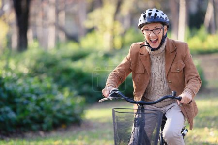 Téléchargez les photos : Femme âgée gaie à vélo dans le parc public. Activités pour les personnes âgées - en image libre de droit