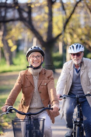 Photo for Cheerful active senior couple with bicycles in public park together having fun. Perfect activities for elderly people. Happy mature couple riding bicycles in park - Royalty Free Image