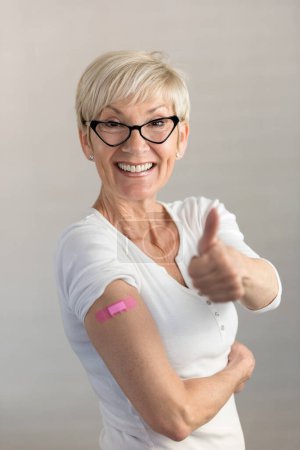 Téléchargez les photos : Portrait d'une belle femme âgée qui vient de se faire vacciner avec les pouces levés - en image libre de droit