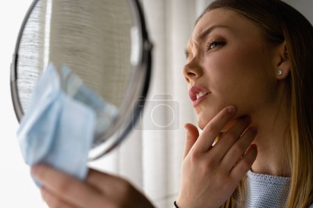 Photo for Young beautiful woman looking herself in the mirror at home. Worried about acne . Problems with acne. - Royalty Free Image