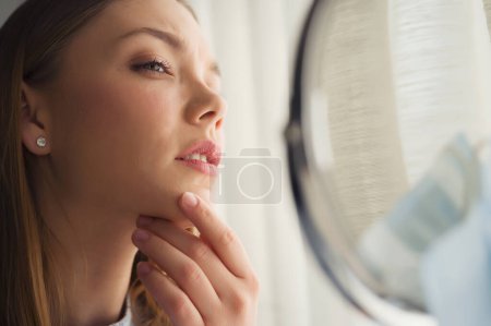 Foto de Joven mujer hermosa mirándose en el espejo en casa. Preocupado por el acné. Problemas con el acné. - Imagen libre de derechos