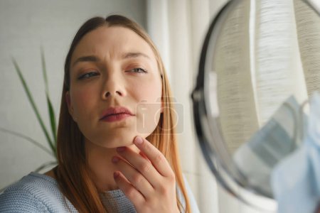 Photo for Young beautiful woman looking herself in the mirror at home. Worried about acne . Problems with acne. - Royalty Free Image