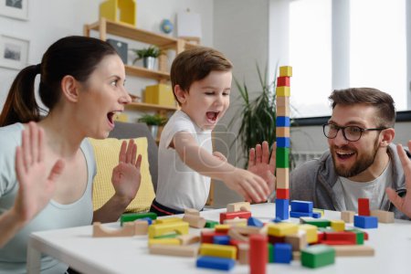 Photo for Young happy family. Mother and father playing with her cute toddler son at home using didactic wooden toys. Home education - Royalty Free Image