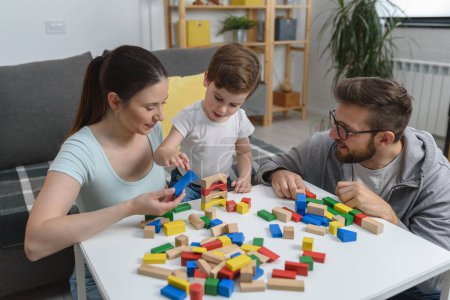 Foto de Joven familia feliz. Madre y padre jugando con su lindo hijo pequeño en casa usando juguetes didácticos de madera. Educación en el hogar - Imagen libre de derechos