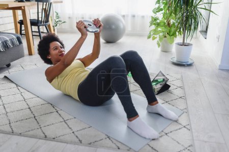 Photo for African-American woman doing exercises on the floor at her home. Trying to stay healthy and fit. - Royalty Free Image