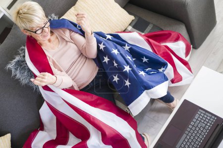 Téléchargez les photos : Vieille dame américaine regardant des jeux, acclamant avec un drapeau américain soutenant son équipe. - en image libre de droit