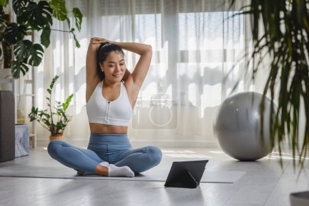 Foto de Hermosa joven haciendo ejercicios de yoga en la estera en la sala de estar - Imagen libre de derechos