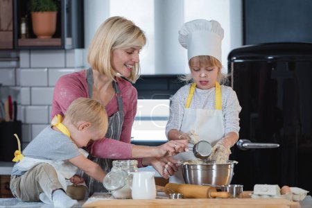 Téléchargez les photos : Mère heureuse cuisine avec fille et fils - en image libre de droit