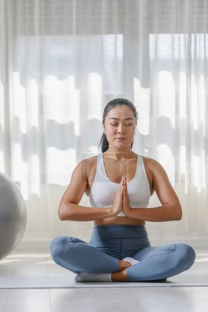 Foto de Mujer asiática joven practicando ejercicio de yoga en casa. Rutinas deportivas diarias para un estilo de vida saludable y alivio del estrés. - Imagen libre de derechos
