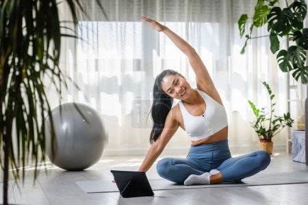 Téléchargez les photos : Jeune femme asiatique instructeur de yoga en utilisant tablette PC sur un cours de yoga en ligne - en image libre de droit