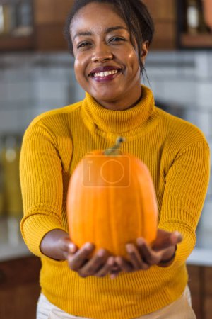 Photo for Young smiling black woman preparing for Halloween carving a pumpkin at home in the kitchen - Royalty Free Image