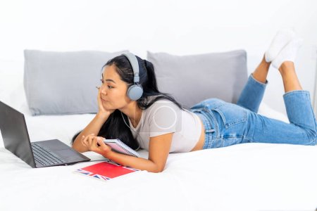 Photo for Asian student, a young woman learning the English language over the internet at home. Using headphones and a laptop computer, attending an online class - Royalty Free Image