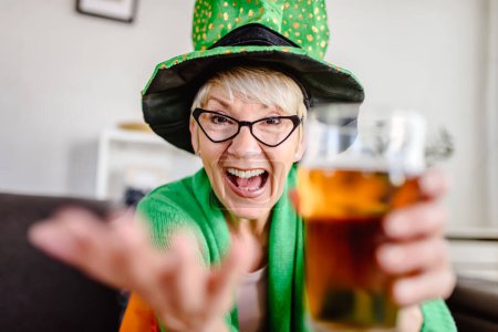 Foto de Vieja irlandesa vistiendo símbolos irlandeses bebiendo cerveza, brindando hacia la cámara - Imagen libre de derechos