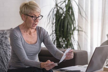 Téléchargez les photos : Femme retraitée âgée travaillant sur un ordinateur à la maison, calculant les dépenses mensuelles, les versements hypothécaires, faisant le budget de la maison - en image libre de droit