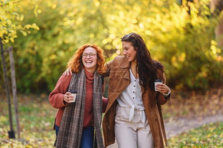 Téléchargez les photos : Deux belles femmes marchant à l'extérieur avec du café - en image libre de droit