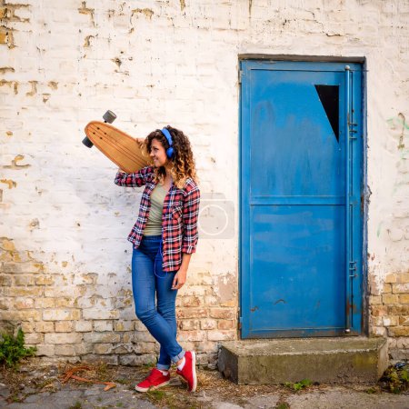 Téléchargez les photos : Jeune fille avec planche à roulettes dans les écouteurs dans la rue - en image libre de droit
