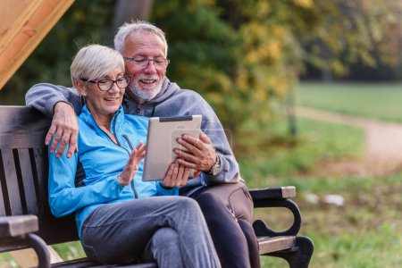 Téléchargez les photos : Couple aîné avec tablette sur banc dans le parc - en image libre de droit