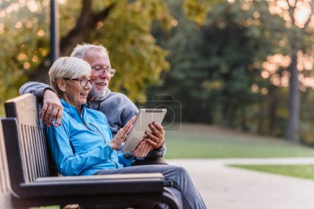 Photo for Senior couple with tablet on bench in park - Royalty Free Image