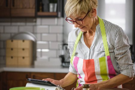 Photo for Beautiful senior woman reading recipe on tablet - Royalty Free Image