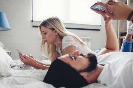 Téléchargez les photos : Couple couché dans le lit avec des téléphones - en image libre de droit