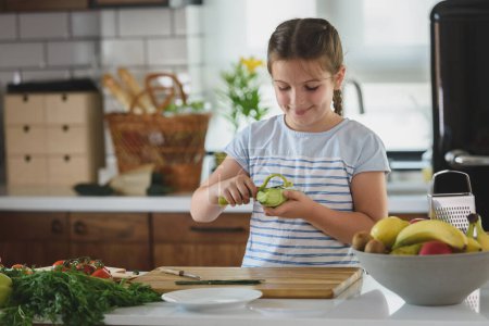 Téléchargez les photos : Jeune jolie fille aider dans la cuisine à préparer un repas végétarien sain - en image libre de droit