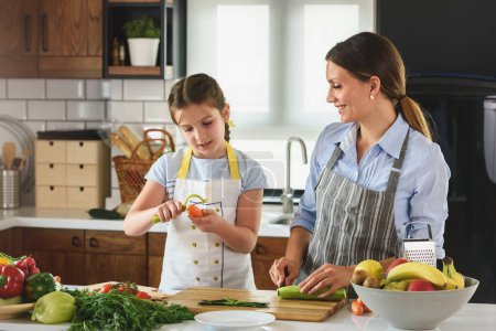 Foto de La linda niña ayudando a la madre en la cocina preparando una sabrosa comida vegetariana - Imagen libre de derechos
