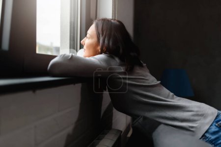 Téléchargez les photos : Femme assise seule à la maison regardant par la fenêtre - en image libre de droit