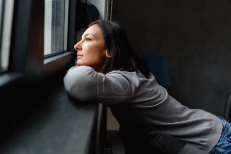 Téléchargez les photos : Femme assise seule à la maison regardant par la fenêtre - en image libre de droit