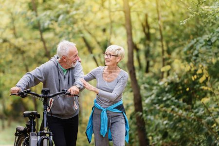 Téléchargez les photos : Joyeux couple de personnes âgées actives avec vélo marchant dans le parc ensemble. Activités parfaites pour les personnes âgées. - en image libre de droit